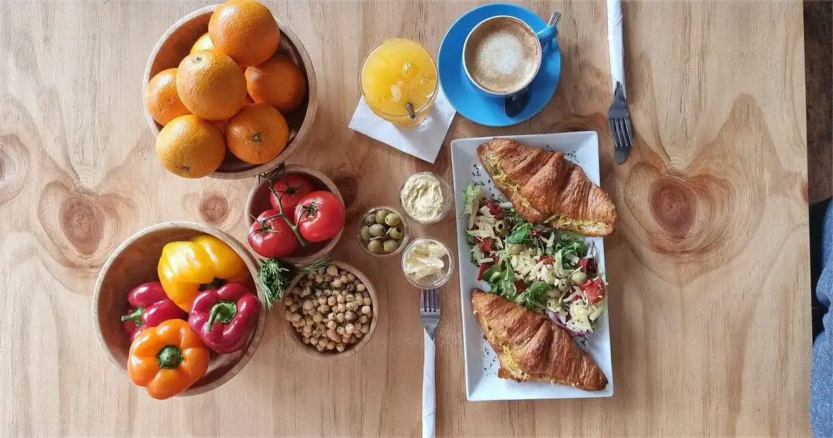 Filled croissants, salad, orange juice and a cappuccino on a wooden table
